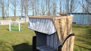 A wicker outdoor seating area with a bench and a table, surrounded by a grassy field and trees. - Wohnung in Wiek nahe Strand Juliusruh (Wiek auf Rügen)