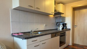 A compact kitchen with white cabinets, a stainless steel sink, and a coffee maker. - Wohnung in Wiek nahe Strand Juliusruh (Wiek auf Rügen)