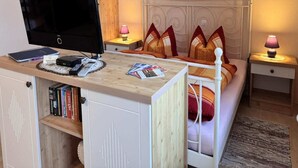 A bedroom with a bed, a TV, a desk with books and a lamp, and a wardrobe. - Wohnung in Wiek nahe Strand Juliusruh (Wiek auf Rügen)