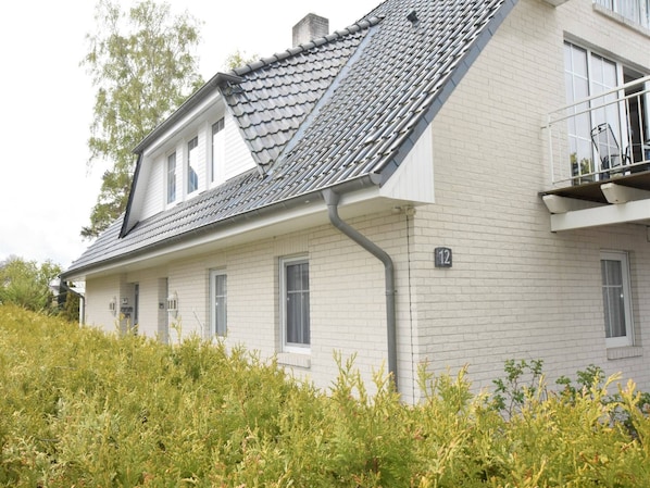 Et toetagers hus med grå tagsten, hvide mursten og en balkon med gelænder.
