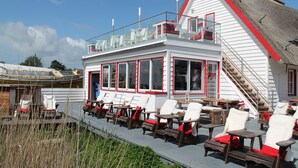 A white building with red trim and a sloped roof. It has multiple windows and a staircase leading to an upper level.