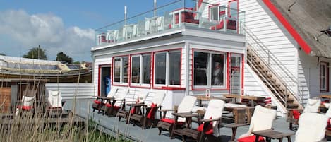 A white building with red trim and a sloped roof. It has multiple windows and a staircase leading to an upper level.