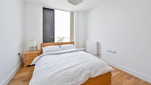 Een minimalistische slaapkamer met een houten bed, een nachtkastje, een lamp, een raam met gordijnen en een radiator.