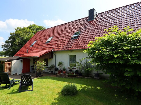 A house with a red-tiled roof, a small porch, and potted plants.