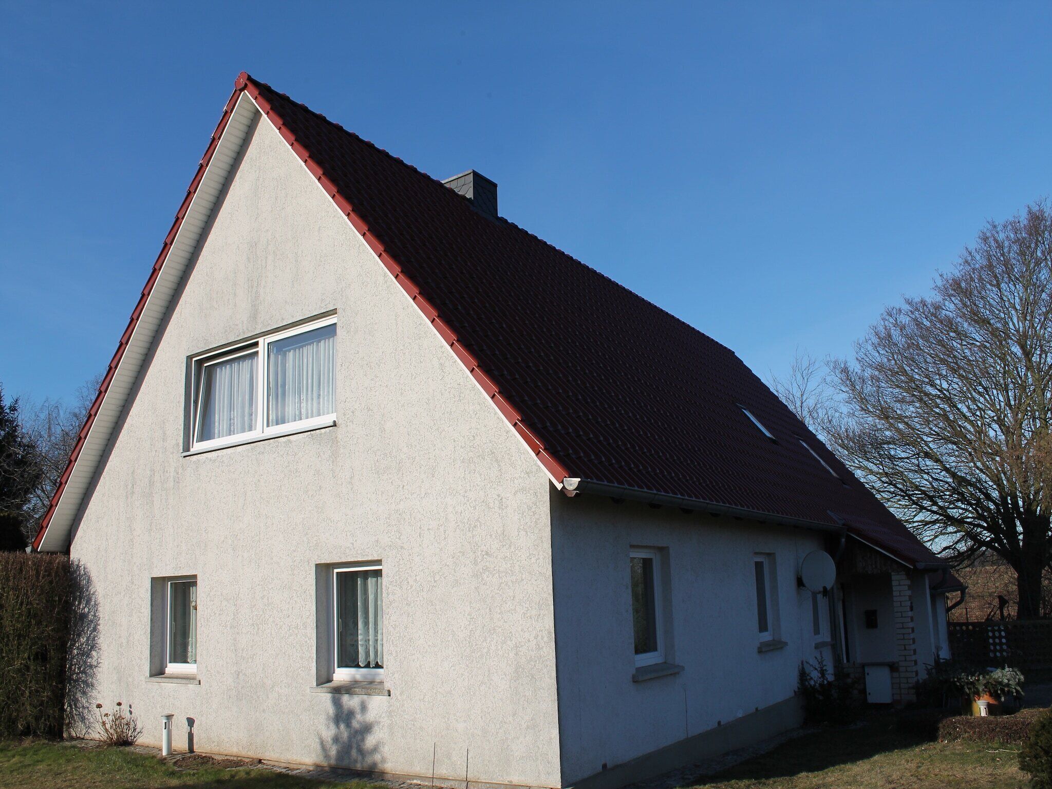 A two-story house with a red roof, a small porch, and a visible satellite dish.