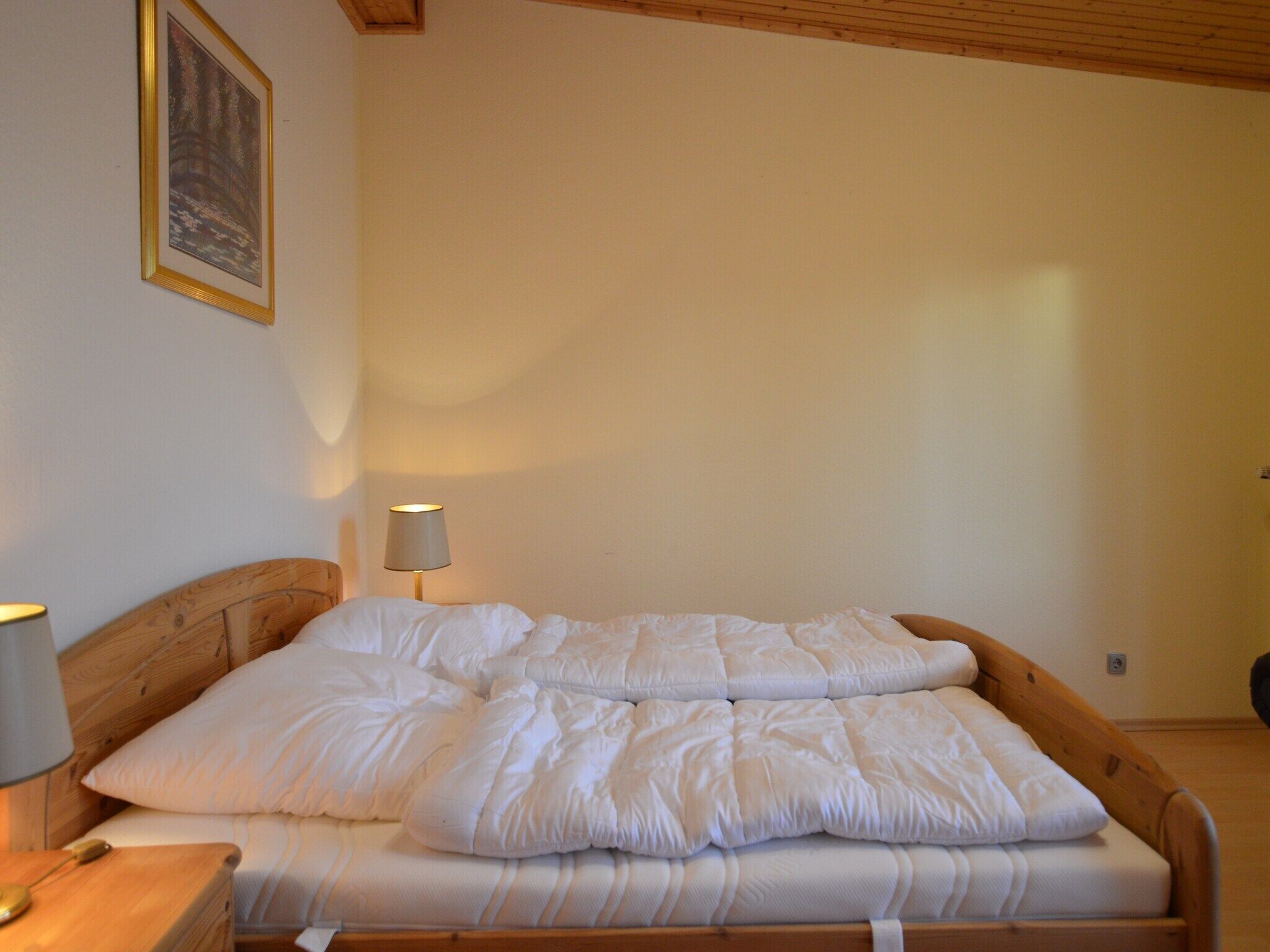 Una cama bien hecha con ropa blanca en una habitación con vigas de madera en el techo.