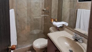 Un baño moderno con cabina de ducha de vidrio, un inodoro, un lavamanos con espejo y un perchero para toallas.