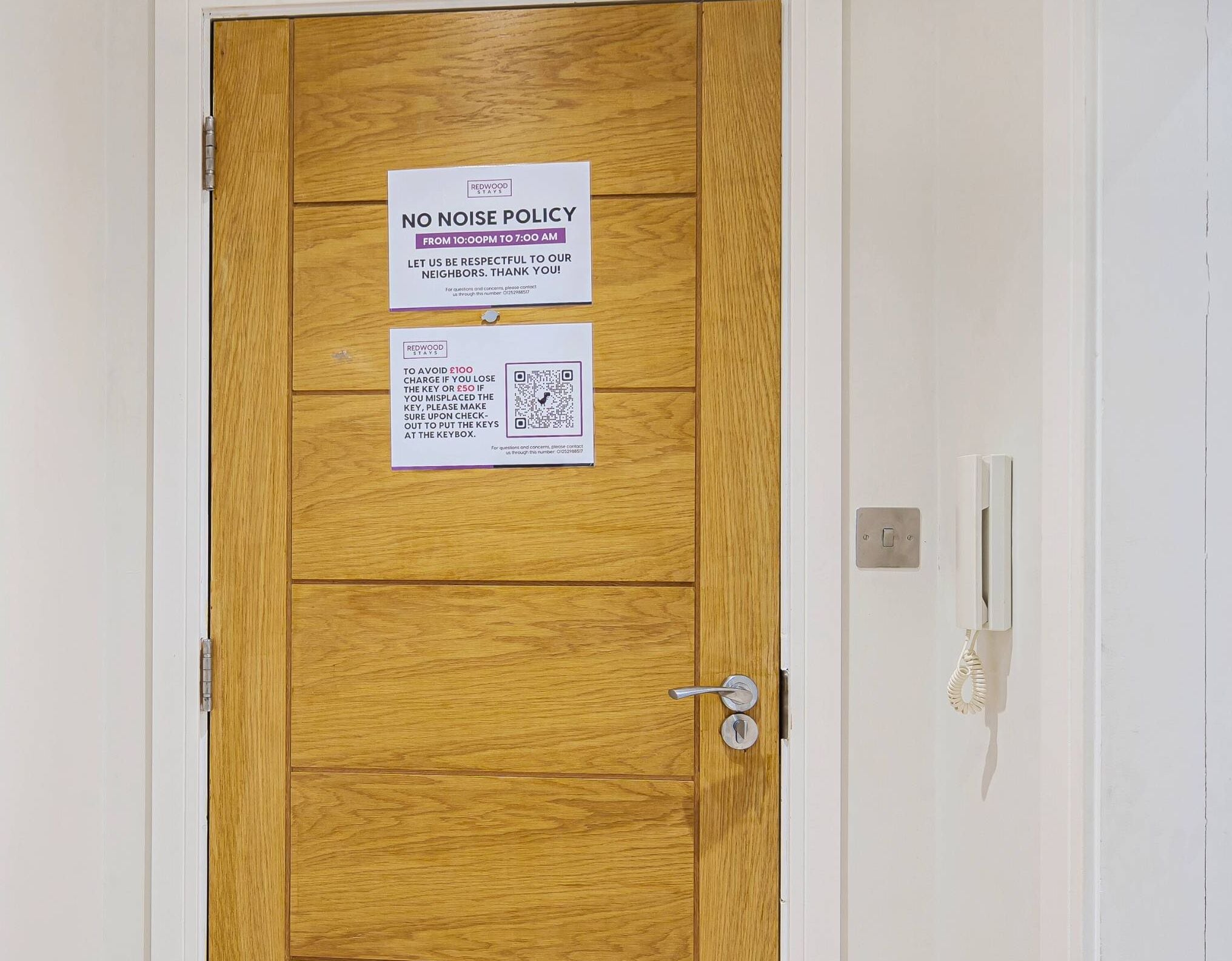 Une porte en bois avec deux panneaux : l’un indiquant une « RÈGLE DE SILENCE » de 22 h 00 à 7 h 00, et l’autre avertissant qu’une somme de 100 £ sera facturée en cas de perte de clés ou une amende de 50 £ en cas de simple égarement, avec un code QR pour obtenir de plus amples informations.