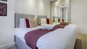A hotel room with two beds, a large mirror, and a wooden floor. - Ragan Court Apartments in Aldershot (Aldershot)