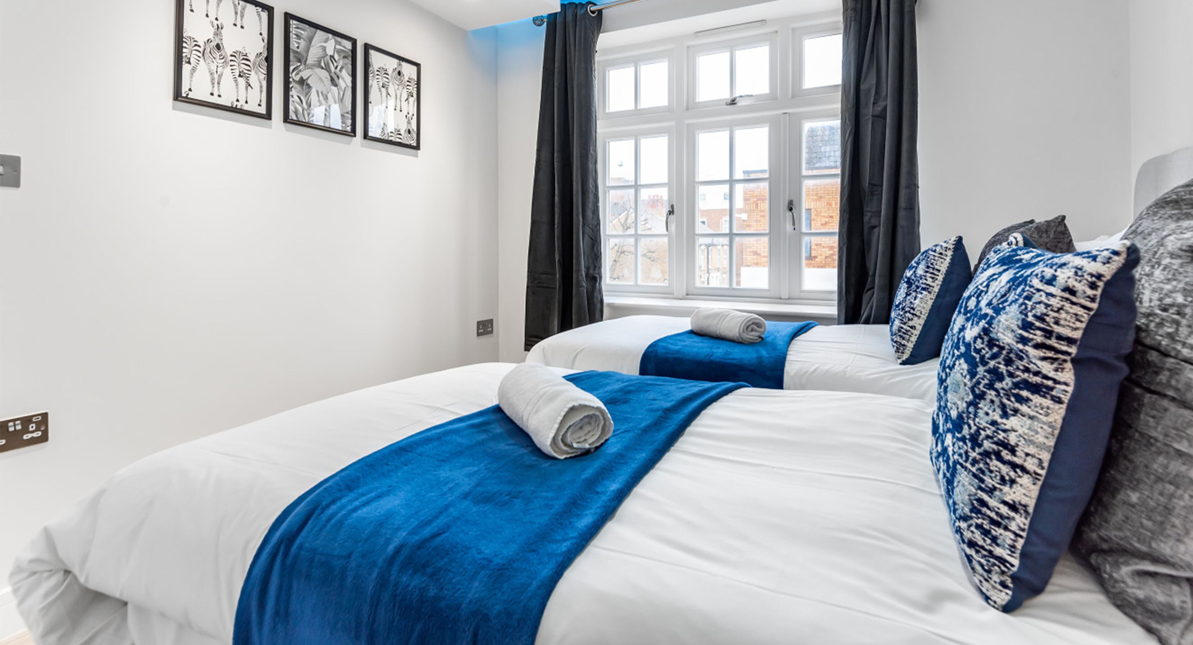 A hotel room with two beds, a window with curtains, and artwork on the wall.