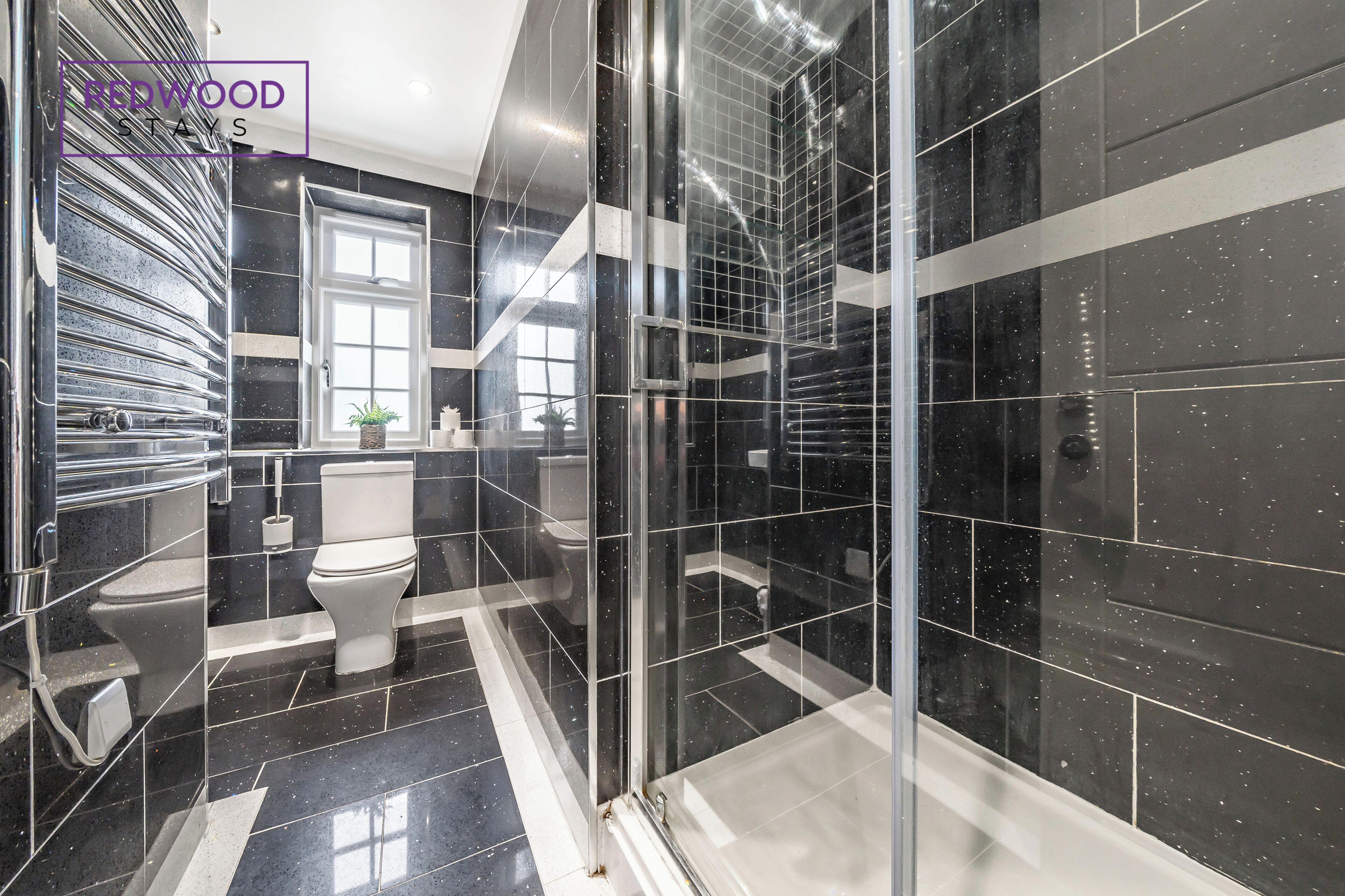 A modern bathroom with black and white tiles, a glass shower enclosure, and a toilet.