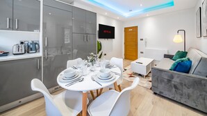 A modern, well-lit room with a dining area, a sofa, and a TV displaying 'NETFLIX'. - Ragan Court Apartments in Aldershot (Aldershot)