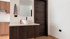 Un baño moderno con un lavabo blanco, muebles de madera oscura, un espejo y una toalla colgada en la pared.