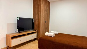 Un dormitorio con un armario de madera, un televisor sobre un mueble de madera y una cama con cubierta marrón.