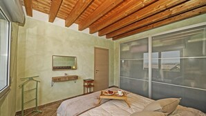 A bedroom with a wooden ceiling, a bed with a beige comforter, a wooden tray with pastries, and a window with a view. - Condominio San Francesco 53 by Wonderful Italy (Desenzano del Garda)