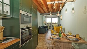 A kitchen with green cabinets, stainless steel appliances, a dining table set with plates, glasses, and a bottle. - Condominio San Francesco 53 by Wonderful Italy (Desenzano del Garda)