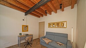 A room with a wooden ceiling, a desk with a chair, a blue sofa, and a door. - Condominio San Francesco 53 by Wonderful Italy (Desenzano del Garda)
