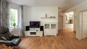 A modern living room with a leather chair, a TV, a cabinet, and a kitchen visible through an open door. - Thale Comfort with Garden (Thale)