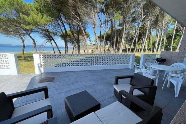 Un patio exterior con asientos, una mesa y vistas al mar y a los árboles.