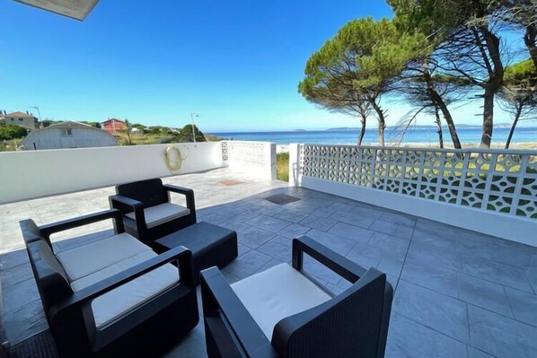Une terrasse dotée de mobilier d’extérieur, d’une clôture blanche décorative et offrant une vue sur la mer et les arbres.