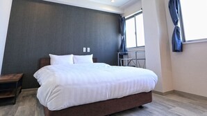 Una habitación de hotel moderna con una cama grande, un escritorio pequeño y un ventanal con cortinas.