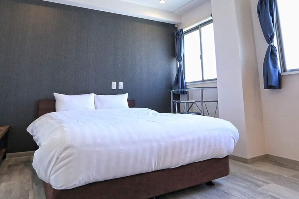 Una habitación de hotel moderna con una cama grande, un escritorio pequeño y un ventanal con cortinas.