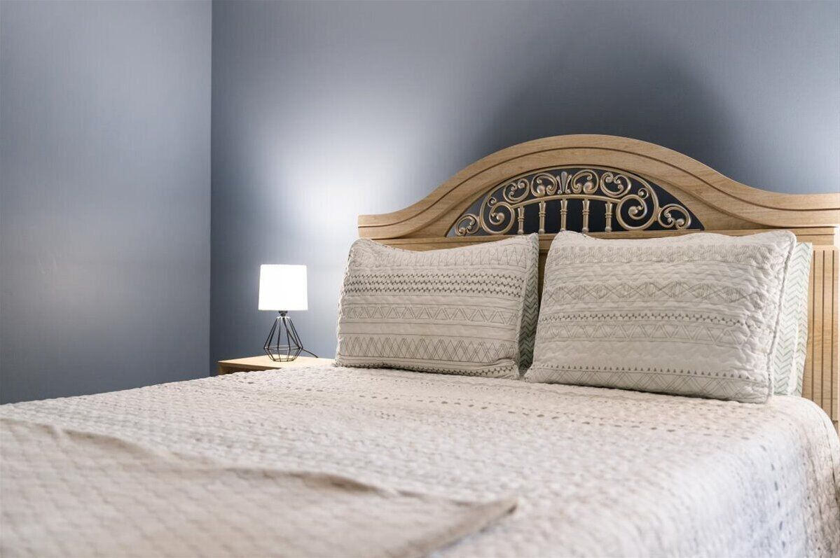 A bed with a wooden headboard, two pillows, and a bedside lamp.