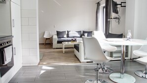 Een moderne keuken met witte kasten, een ingebouwde oven en een eethoek met een glazen tafel en witte stoelen.