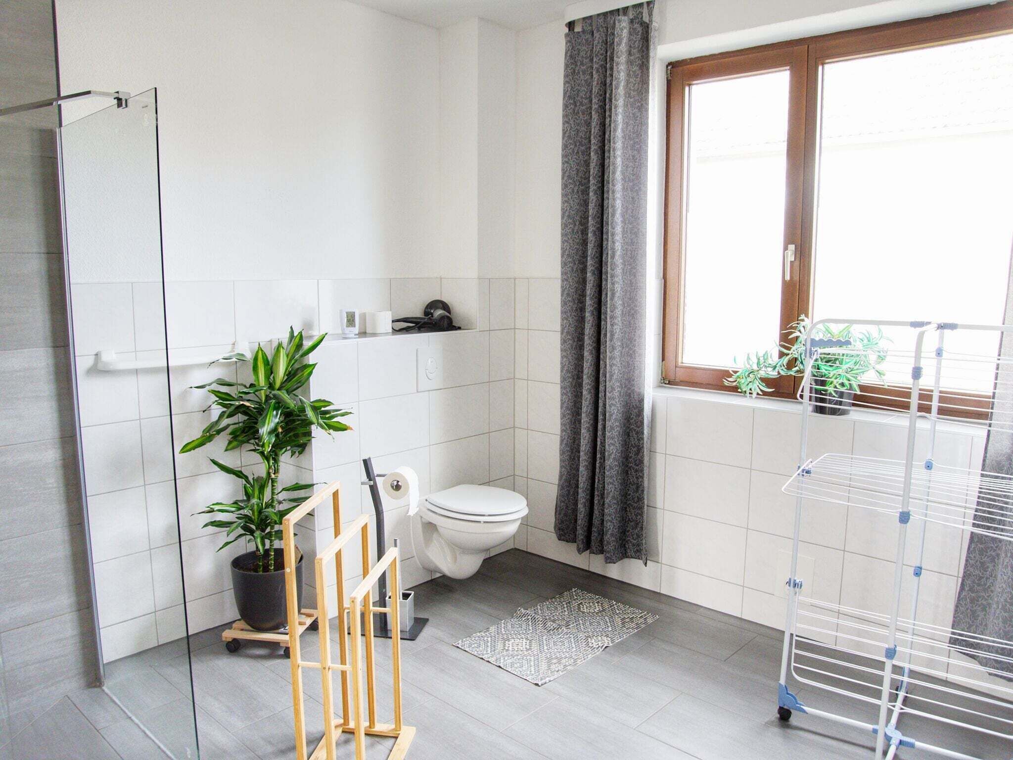 Une salle de bain moderne avec une douche, des toilettes et une fenêtre agrémentée de plantes.