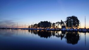 Een jachthaven in de schemering, met rustig water dat boten en bomen weerspiegelt.