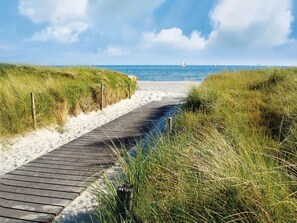 A wooden boardwalk leading to a sandy beach with grassy dunes on either side. - Guest House near Coast (Farve)