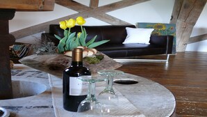A cozy living room with a wooden ceiling, a black sofa with a white pillow, a wooden coffee table with a bottle of wine and two glasses, and a vase with yellow flowers. - Guest House near Coast (Farve)