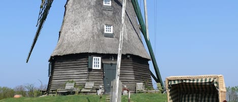 A traditional windmill with a thatched roof, wooden structure, and a small door.