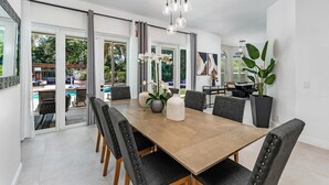A modern dining area with a wooden table, black upholstered chairs, and a large potted plant. - 8BR Entertainers Estate w/ Pool, Games & Theater ! (Coconut Creek)