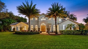 A large, two-story house with a symmetrical facade, multiple windows, and a well-maintained lawn. - 8BR Entertainers Estate w/ Pool, Games & Theater ! (Coconut Creek)
