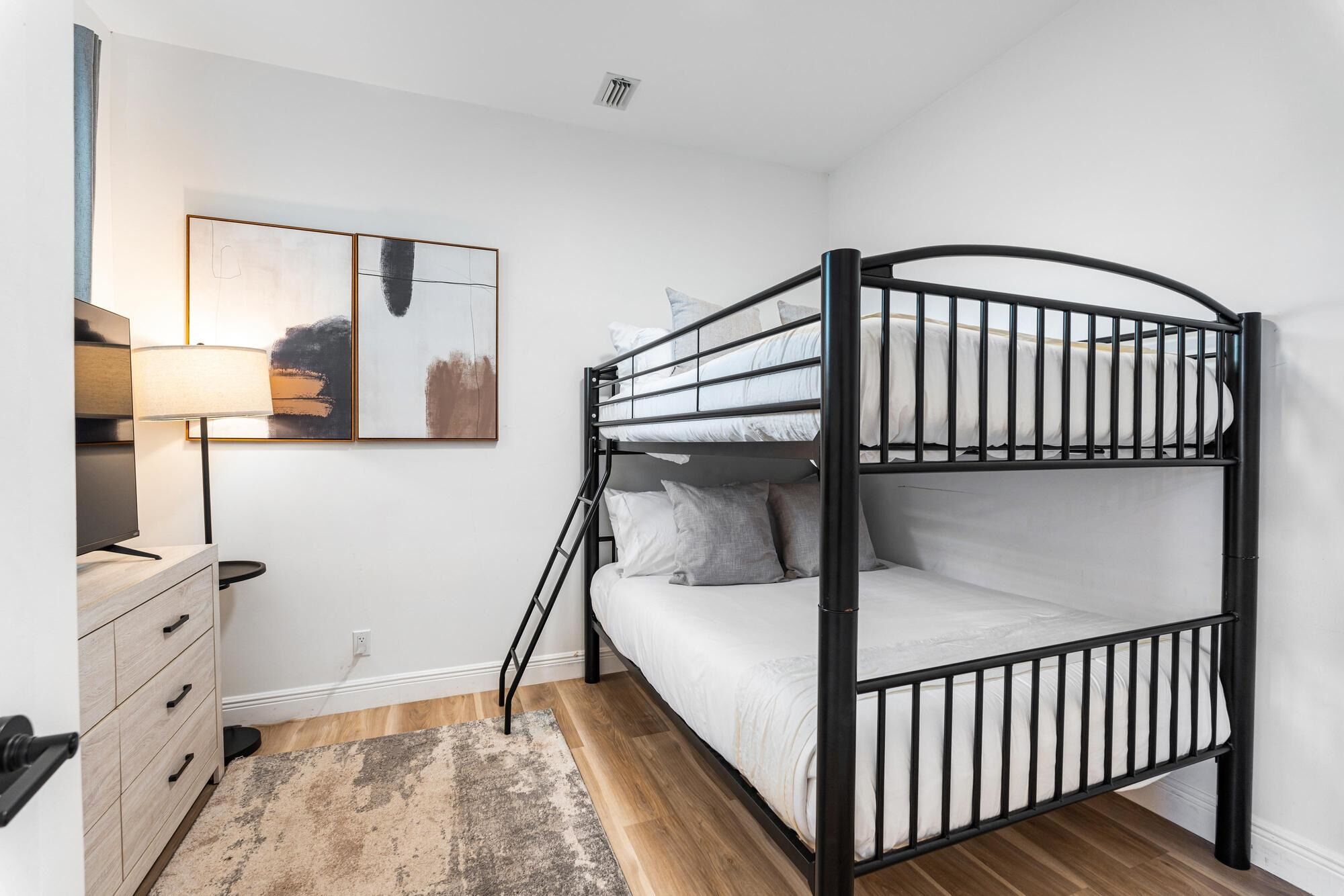 A bunk bed room with a desk, a lamp, and a painting on the wall.