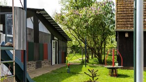 A modern building with a metal exterior, a covered entrance, and a small garden area with a slide and play equipment. - Vacation Home with Pond (Klein Pravtshagen)