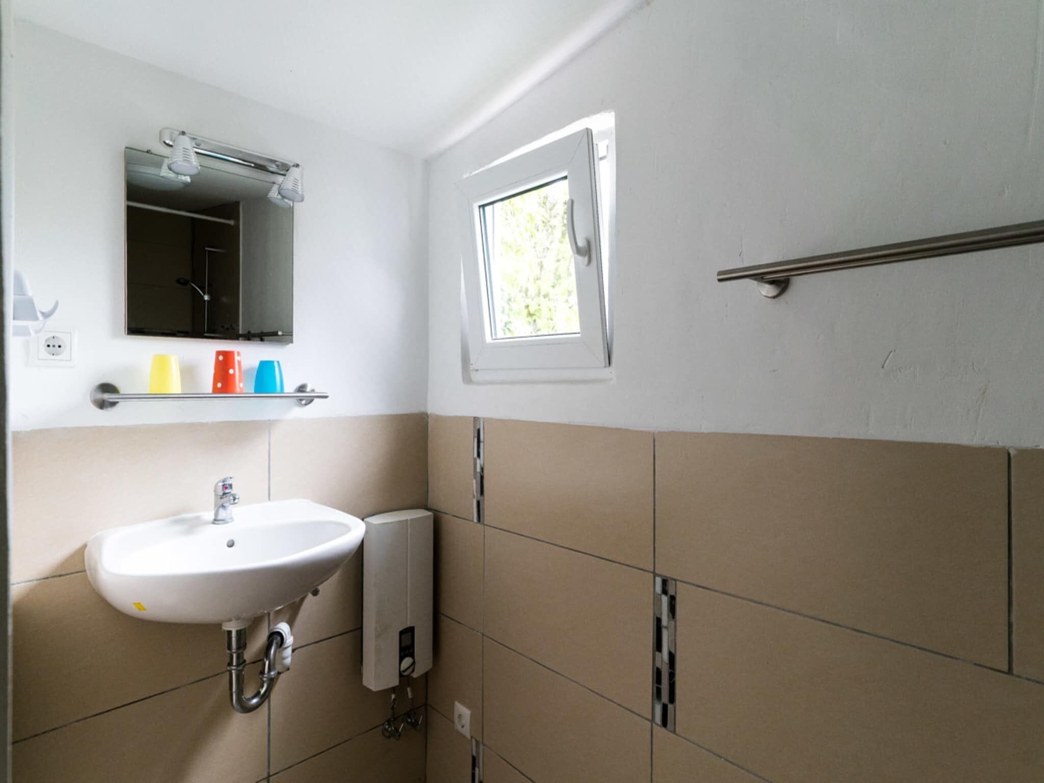 Une salle de bain avec un lavabo blanc, un miroir, une fenêtre et un porte-serviettes.