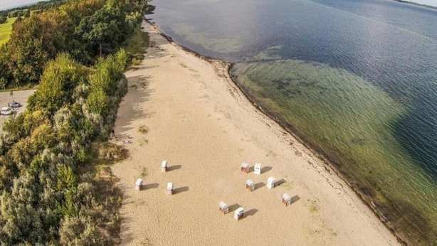 A beach with clear waters, a sandy shore, and several beach huts. - Vacation Home with Pond (Klein Pravtshagen)