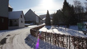 Eine verschneite Landstraße mit Gebäuden an beiden Seiten, darunter ein Stall und ein Haus mit geneigtem Dach.