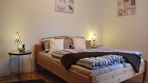 Ein hölzernes Bett mit einer gestreiften Decke, ein Nachttisch mit einer Lampe und ein kleiner Teppich auf dem Boden.