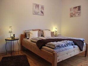 A wooden bed with a striped blanket, a bedside table with a lamp, and a small rug on the floor.