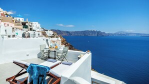 A seaside terrace with white buildings, a table with chairs, and a view of the sea.