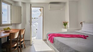 A bedroom with a bed, a desk with chairs, a window, and a door leading outside. - Suite with Caldera View (Santorini)