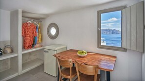 A compact kitchen with a wooden table, two chairs, a small fridge, and a window with a view of the sea. - Suite with Caldera View (Santorini)