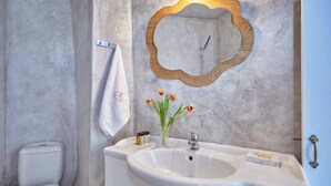 A bathroom with a white sink, a mirror with a wooden frame, a towel hanging on a hook, and a toilet. - Suite with Private Hot Tub (Santorini)