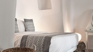 A minimalist bedroom with a bed, a small bedside table, and a wall-mounted light fixture. - Suite with Private Hot Tub (Santorini)