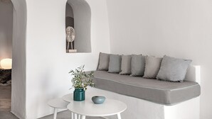 A minimalist interior with a white sofa, a small table, and a decorative vase. - Suite with Private Hot Tub (Santorini)
