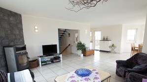 Una sala de estar con chimenea, televisor, sofá, mesa de centro y una escalera que lleva a otra habitación.