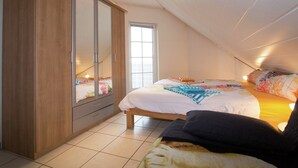 Un dormitorio con un armario grande, una cama con muchos almohadones y una ventana.